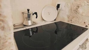 Ett kök med en svart induktionshäll, en kaffebryggare och en vit tallrik på bänkskivan.