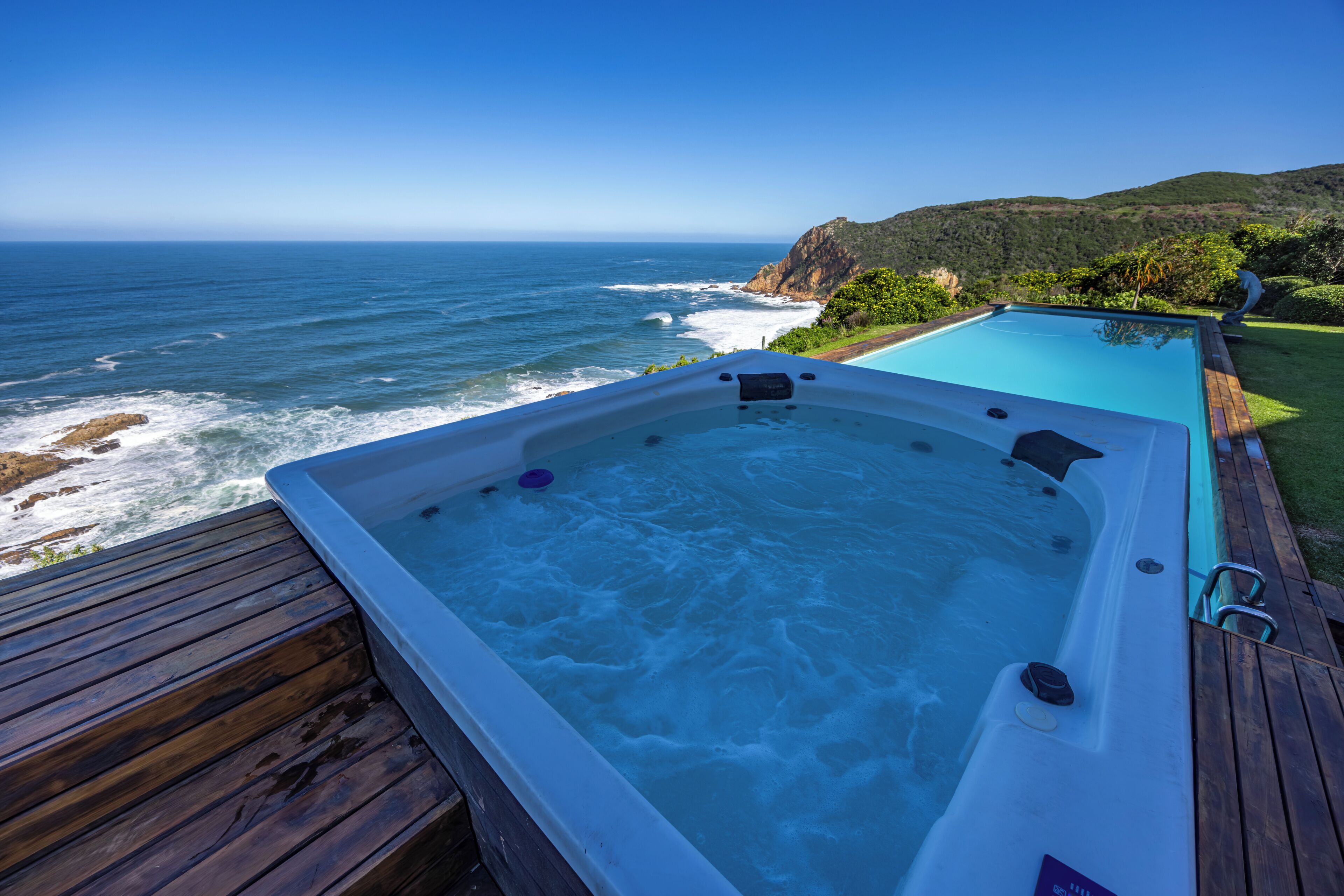 Un bain à remous sur une terrasse en bois, avec vue sur l’océan et les vagues qui se brisent sur le rivage.