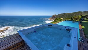 Ein Whirlpool auf einer Holzterrasse mit Blick auf den Ozean, wo Wellen an die Küste brechen.