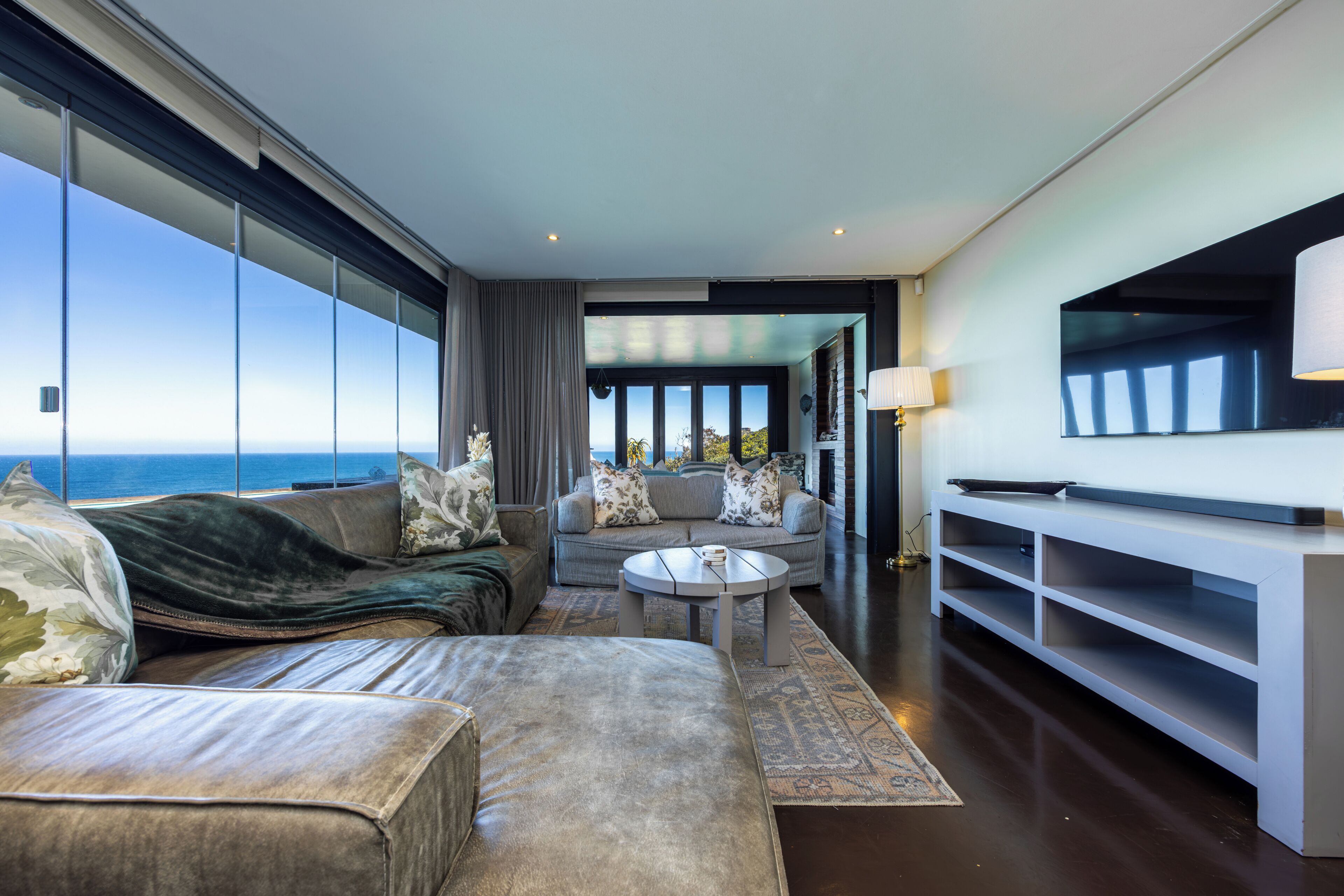 Un salon moderne avec un canapé, un fauteuil et une table basse, un téléviseur fixé au mur et une vue sur la mer.