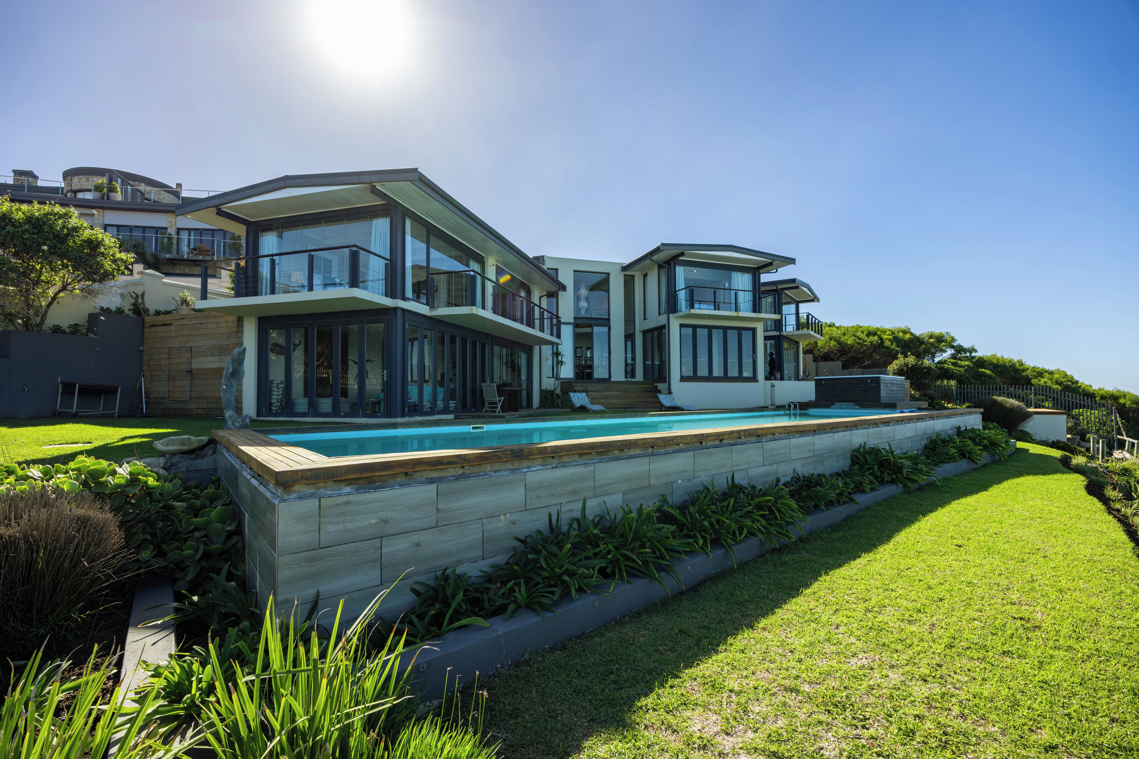 Une maison moderne à plusieurs étages, dotée d’une piscine, de grandes fenêtres et d’une pelouse bien entretenue.