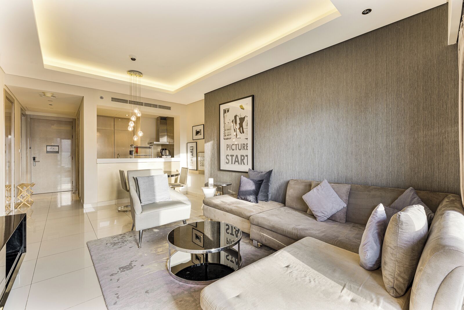 A modern living room with a sofa, armchairs, a coffee table, and a kitchen in the background.