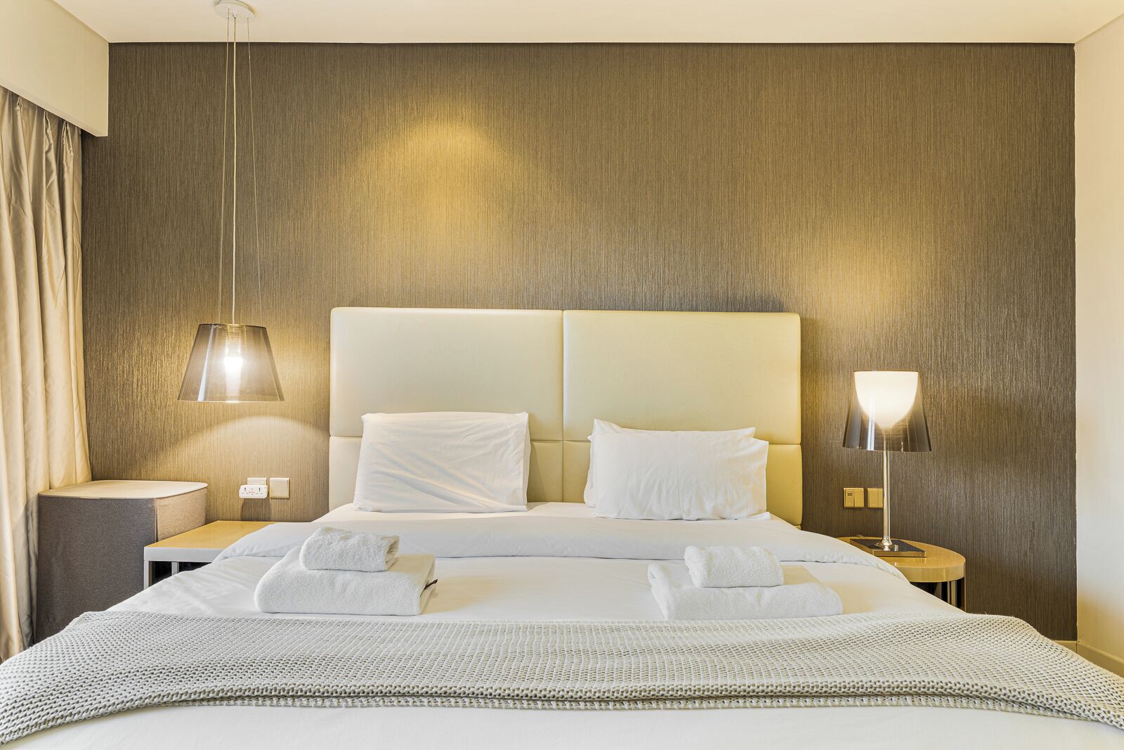 Habitació d'hotel amb un llit gran, dues làmpades de nit, una taula de nit i una làmpada de paret.