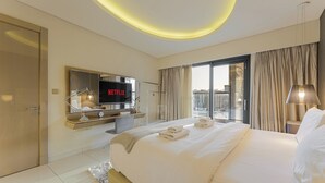 Habitación de hotel con una cama grande, un televisor mostrando 'NETFLIX', un escritorio con una lámpara y vistas a la ciudad a través de amplias ventanas.