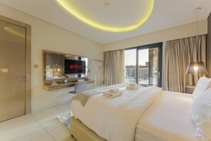 A hotel room with a large bed, a TV displaying 'NETFLIX,' a desk with a lamp, and a view of the city through large windows. - Amazing 1BR, 10 mins to Burj Khalifa (Dubai)