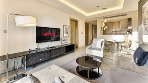 Una sala de estar moderna con un televisor de pantalla plana grande, un sofá, una mesa de centro y un comedor con una cocina al fondo.