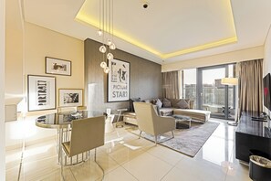 Ein modernes Wohnzimmer mit Sofa, Couchtisch und Essbereich. An der Wand befinden sich gerahmte Bilder und ein großes Fenster mit Vorhängen.