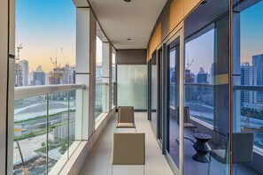 A modern balcony with large windows, a glass railing, and a view of a cityscape with buildings and construction cranes. - Amazing 1BR, 10 mins to Burj Khalifa (Dubai)