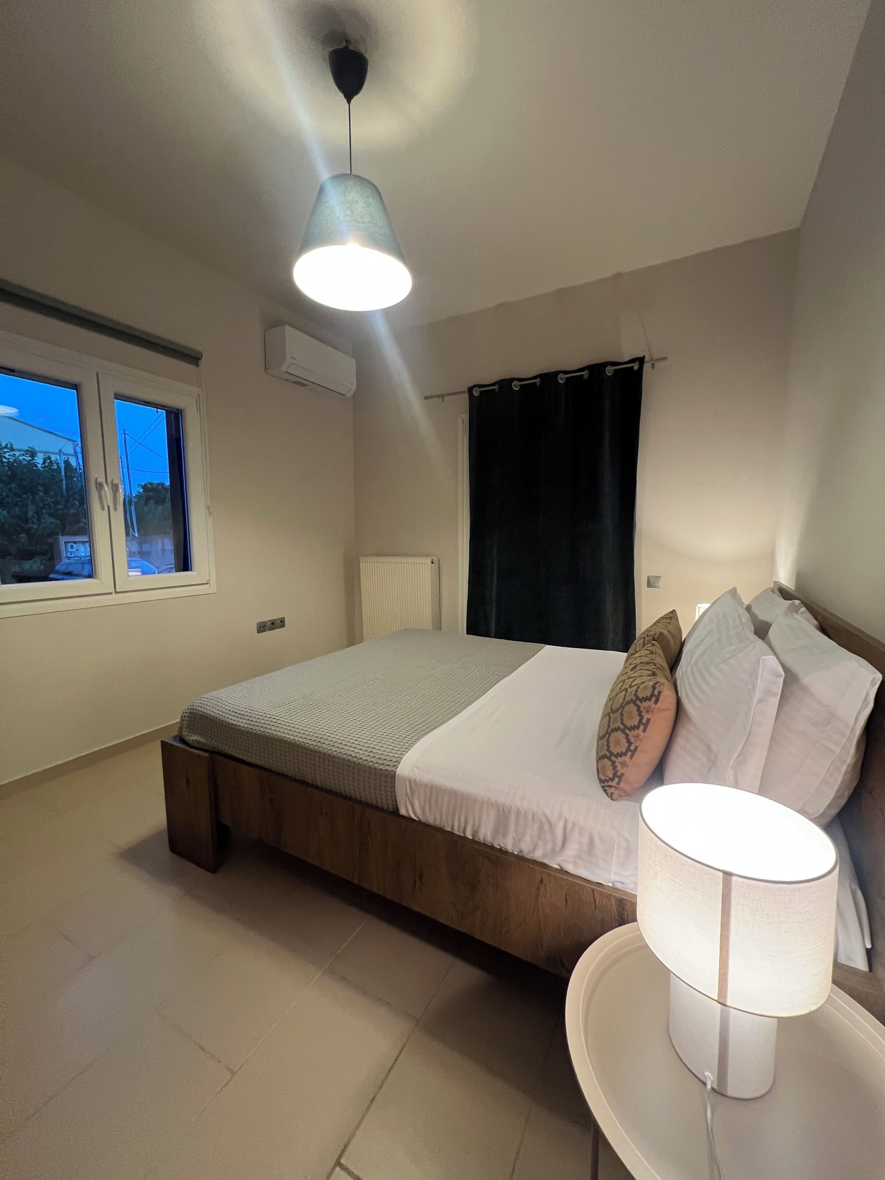 Een slaapkamer met een bed, een bedlampje, een raam en een plafondlamp.