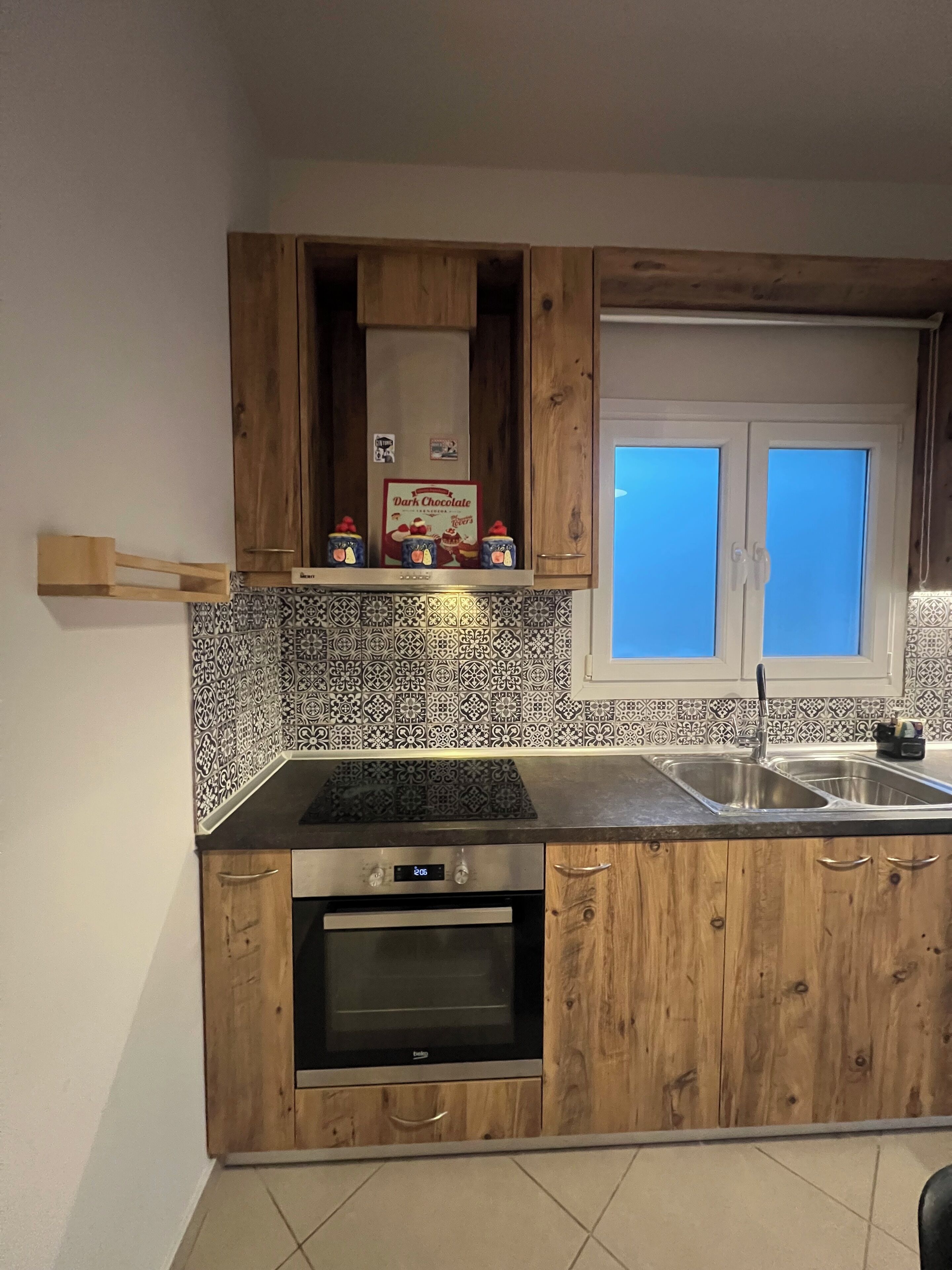 A kitchen with wooden cabinets, a built-in oven, a stainless steel sink, and a window with blinds.