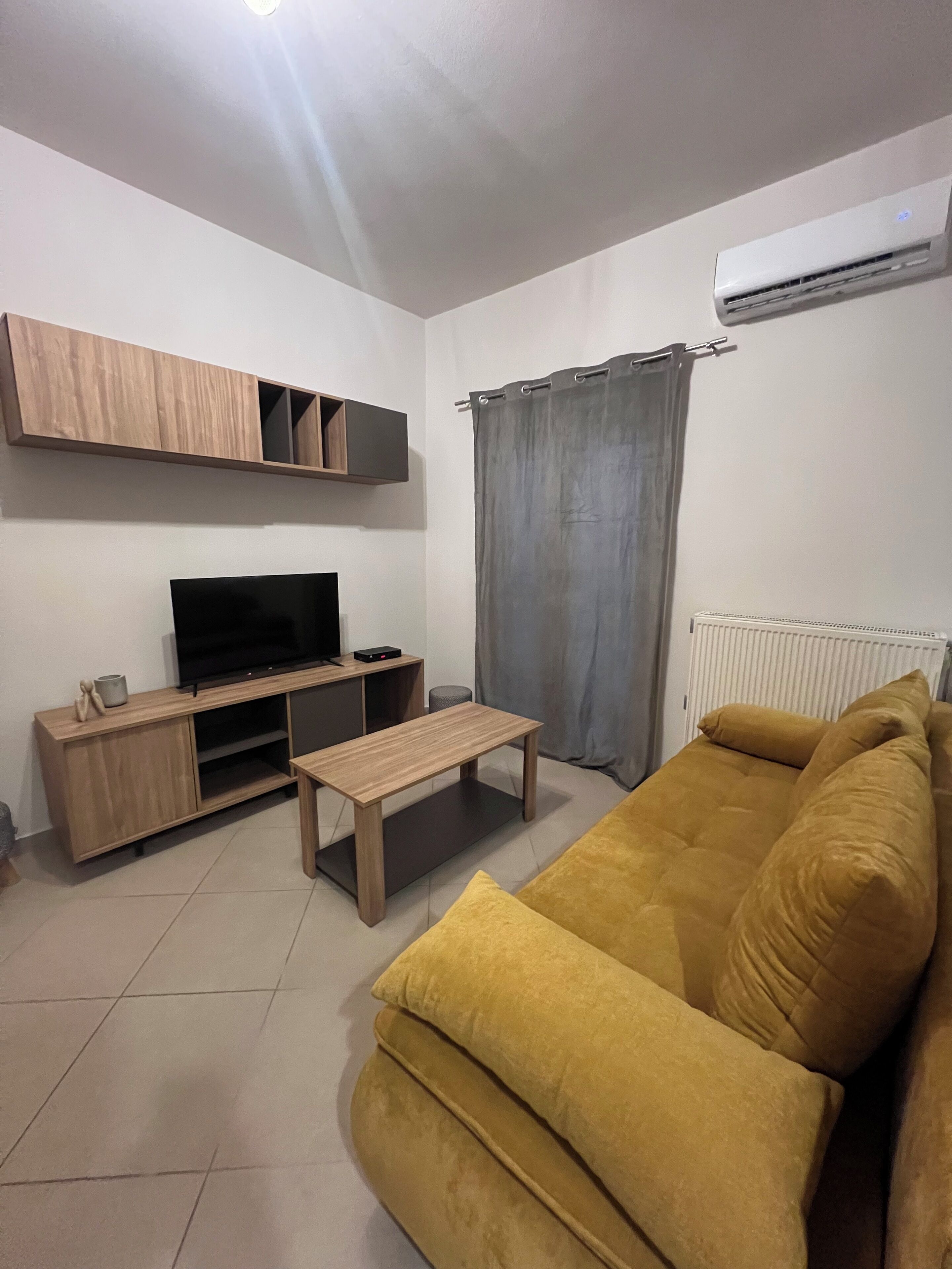 A living room with a sofa, TV, wooden entertainment unit, and a radiator.