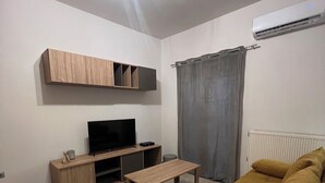 A living room with a sofa, a TV, a coffee table, and a wall-mounted shelf. - ORA Garden Residence (corfu)