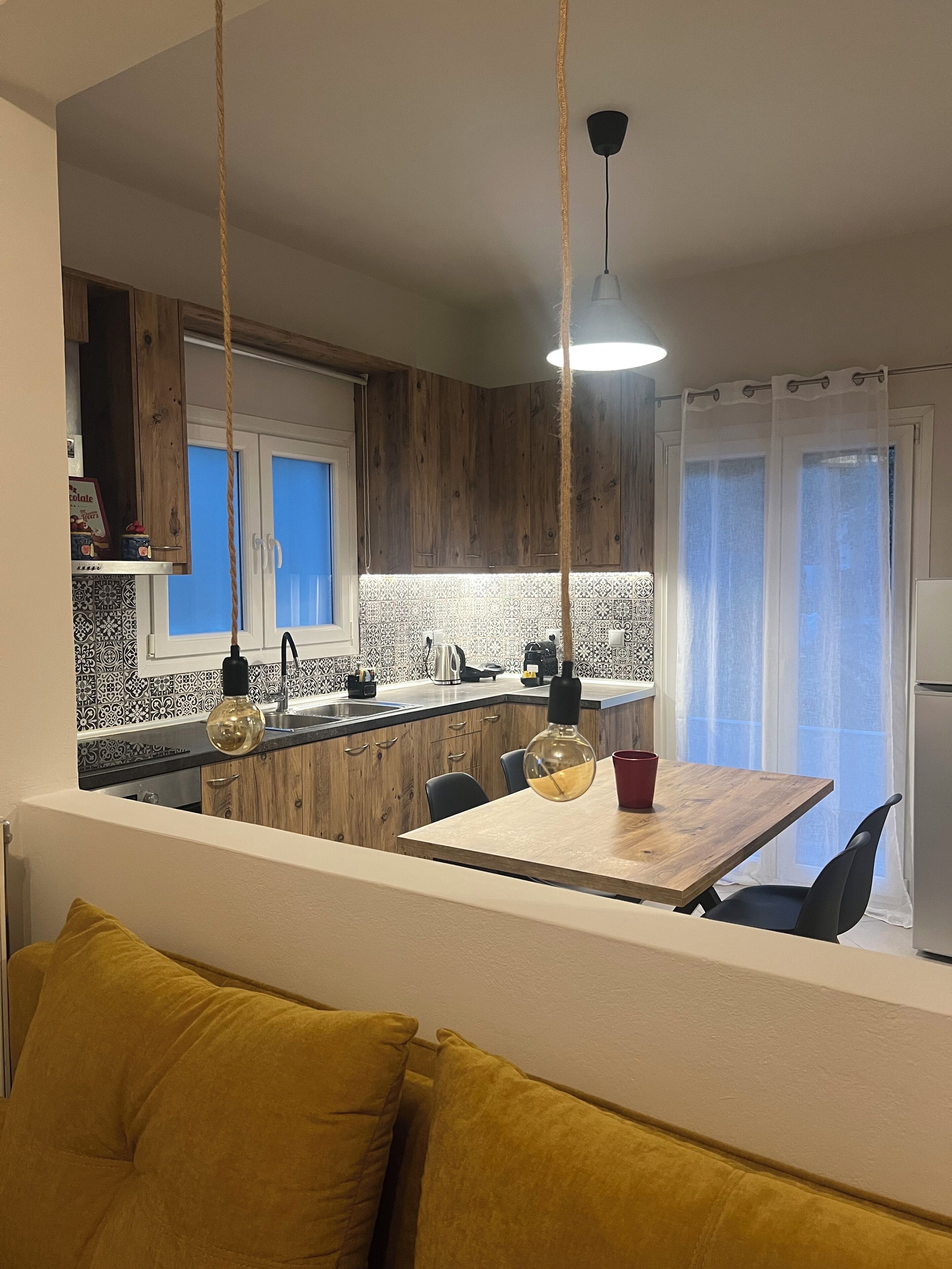 A modern kitchen with wooden cabinets, a dining area with a table and chairs, and a hanging light fixture.