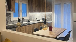 A modern kitchen with wooden cabinets, a dining area with a table and chairs, and a hanging light fixture. - ORA Garden Residence (corfu)