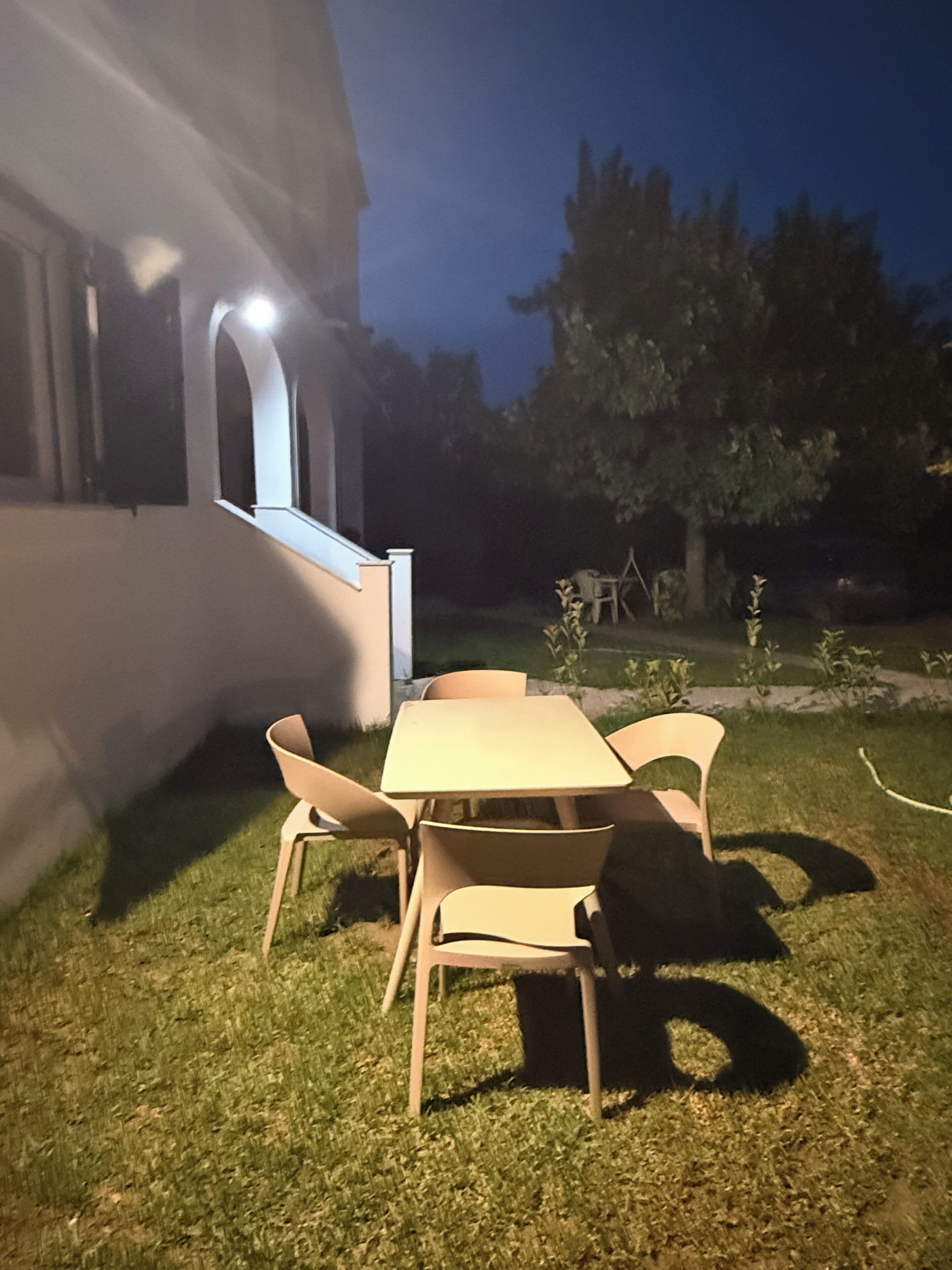 Un espace extérieur aménagé avec une table et des chaises, une pelouse verdoyante et un bâtiment en arrière-plan.
