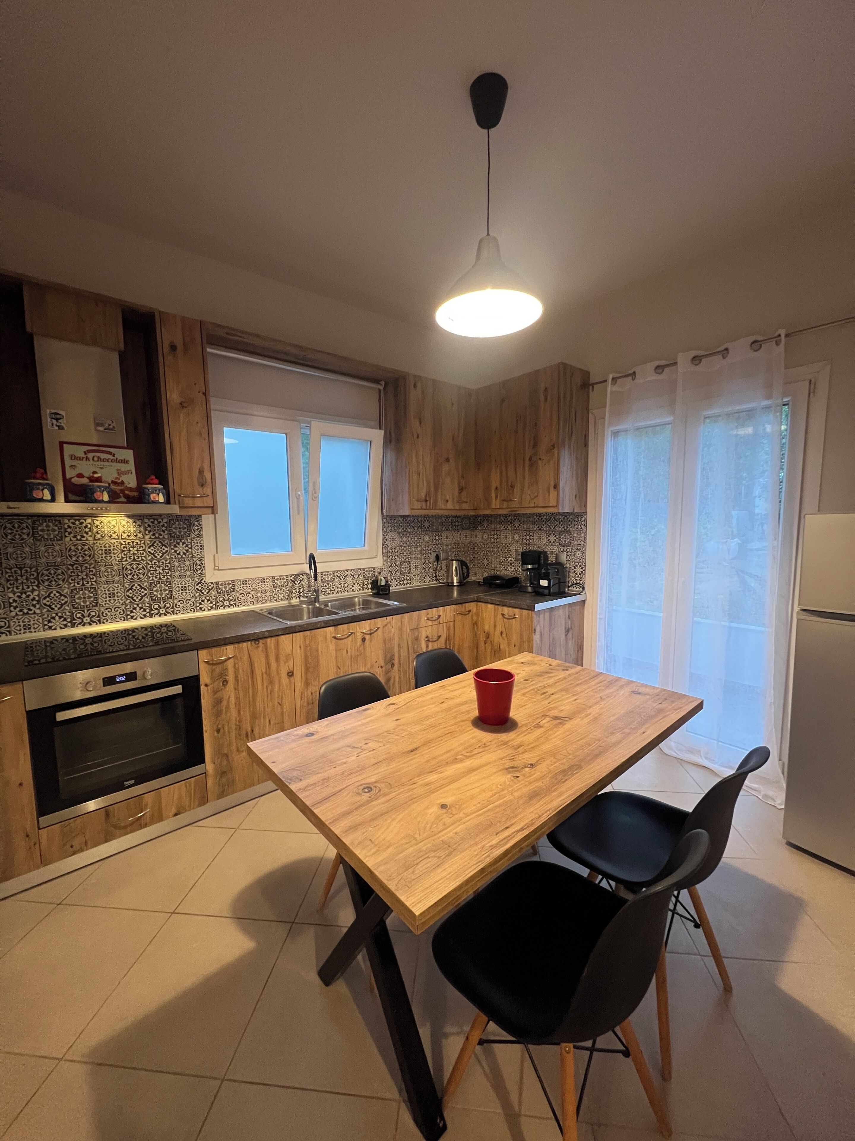 Una cocina moderna con armarios de madera, horno integrado, una mesa de comedor con sillas y una ventana con cortinas.
