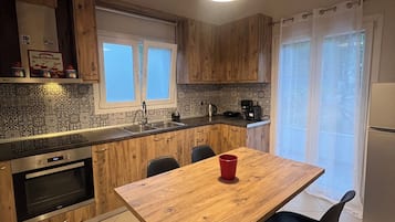 Una cocina moderna con armarios de madera, horno integrado, una mesa de comedor con sillas y una ventana con cortinas.