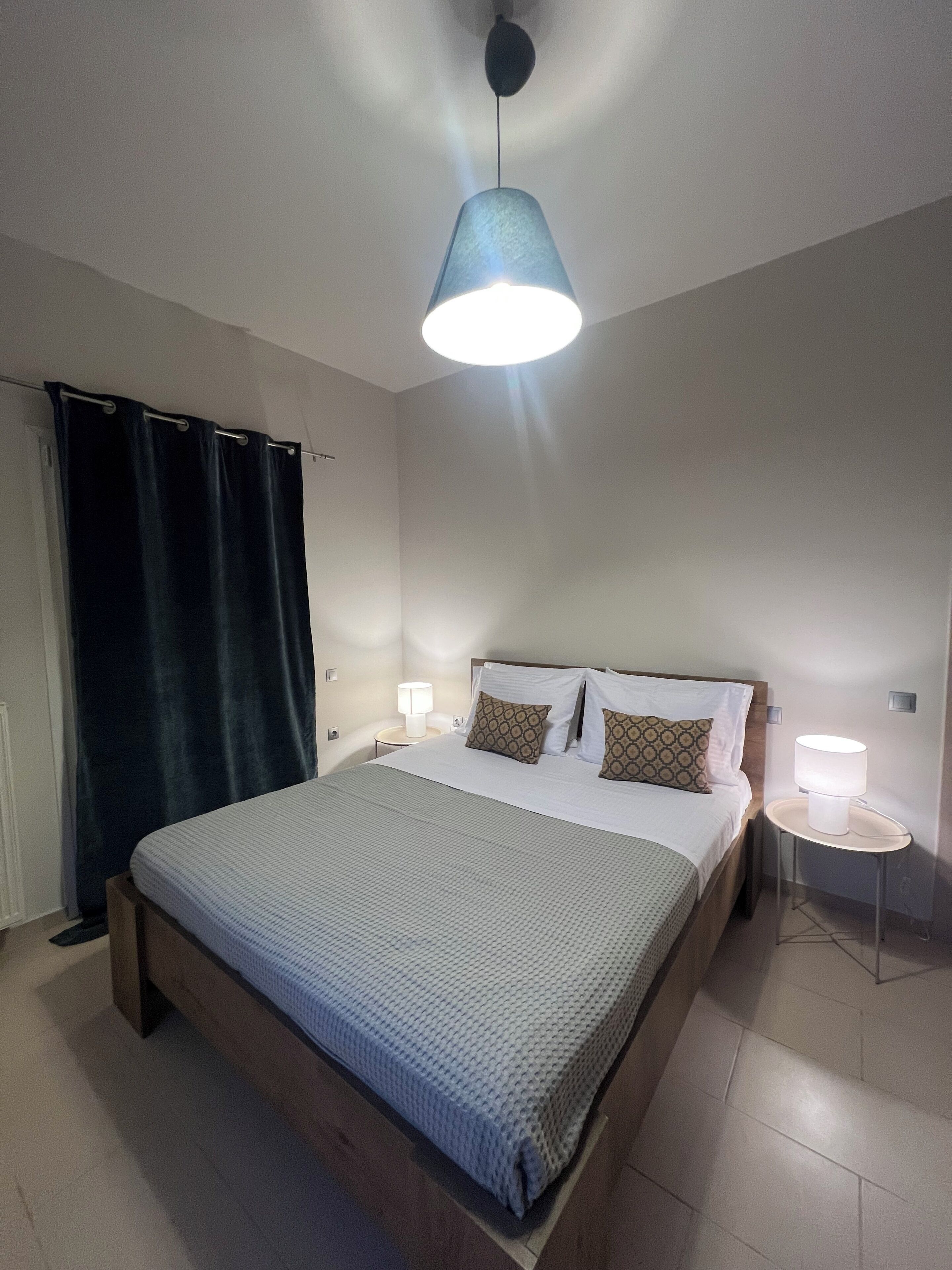 Ein Schlafzimmer mit einem Bett, einem Nachttisch mit Lampe, einer Hängeleuchte und einem Vorhang.