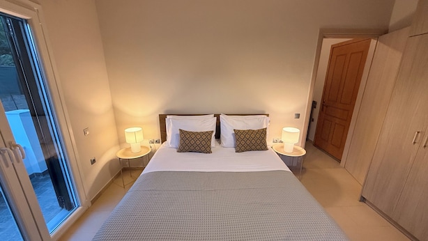 A hotel room with a large bed, two bedside tables with lamps, a wardrobe, and a sliding glass door leading to a balcony. - ORA Garden Residence (corfu)