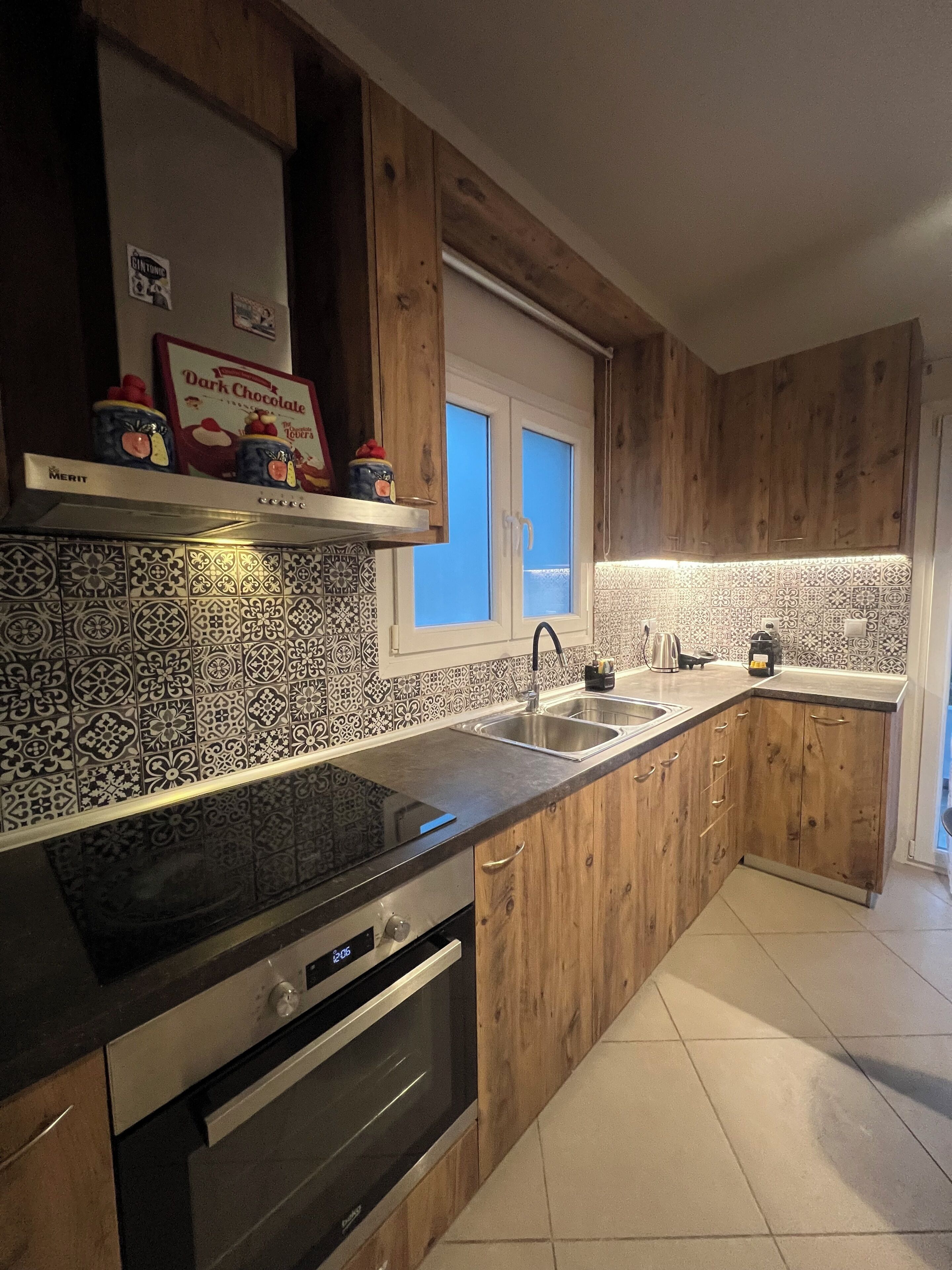 A kitchen with wooden cabinets, a black countertop, a stainless steel sink, and a window above the sink.