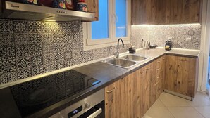 A kitchen with wooden cabinets, a black countertop, a stainless steel sink, and a window above the sink. - ORA Garden Residence (corfu)