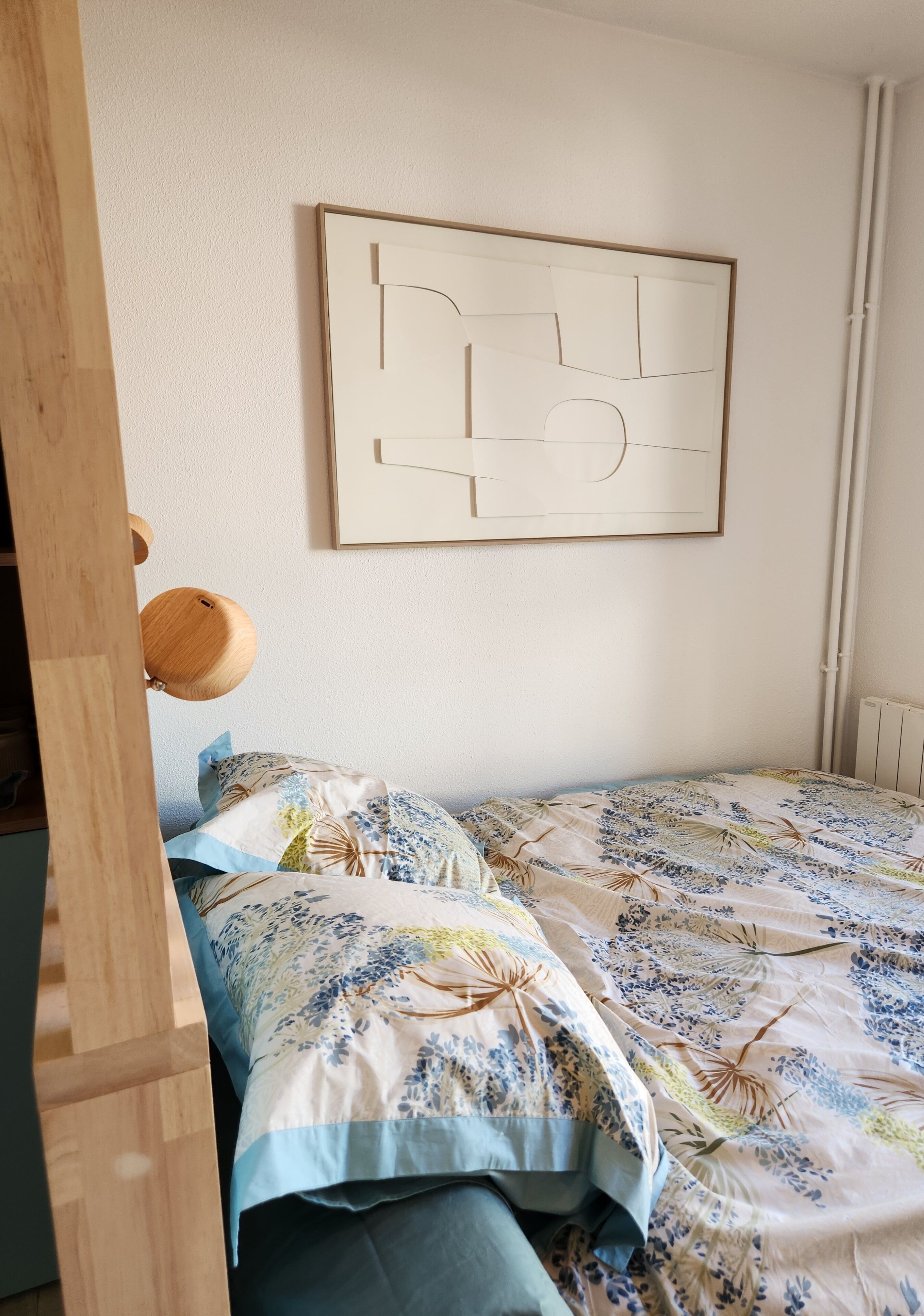 A bedroom with a bed, a wall-mounted abstract painting, and a wooden headboard.