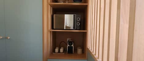 Cocina compacta con microondas, hervidor y estanterías.