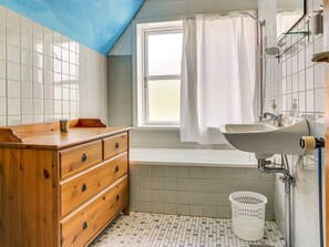 Ein Badezimmer mit einem Holzkosmetikschrank, einem weißen Waschbecken, einer Badewanne und einem Fenster mit Vorhang.