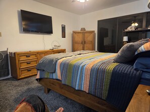 Camera da letto con letto, comò, televisore, armadio e vista su un'altra stanza.