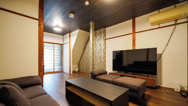 A modern living room with a flat-screen TV, a sofa, a coffee table, and a wooden ceiling. - Guest House WASSO (京都市伏見区深草下川原町)