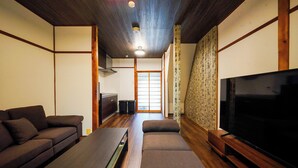 A room with a sofa, a TV, a wooden floor, and a sliding door leading to another room. - Guest House WASSO (京都市伏見区深草下川原町)
