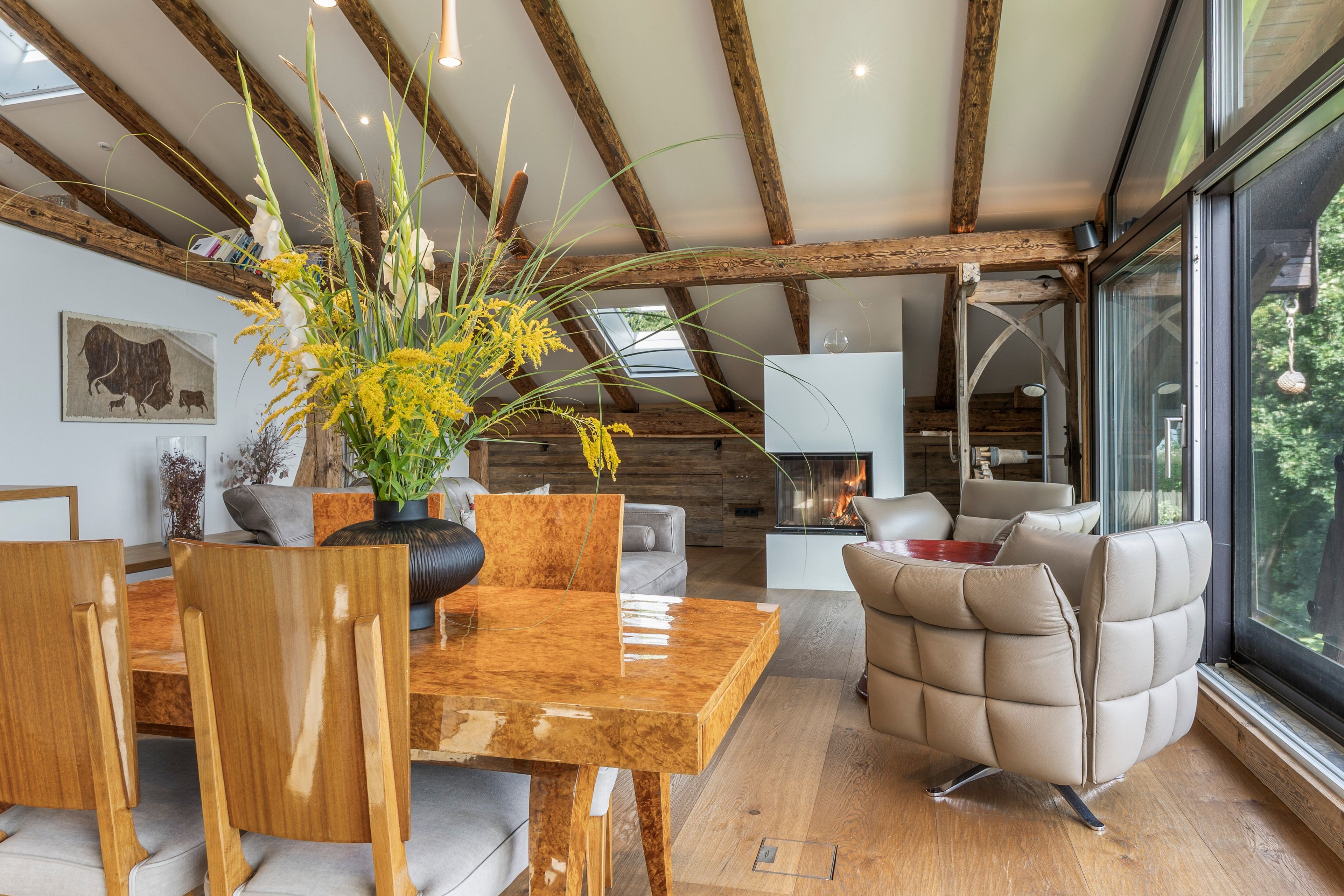 A spacious living area with a wooden dining table, comfortable seating, and a large window offering a view of the outdoors.