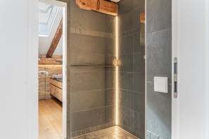 Ein modernes Badezimmer mit dunklen Fliesen, einer Holzbalkendecke und einem Oberlicht.