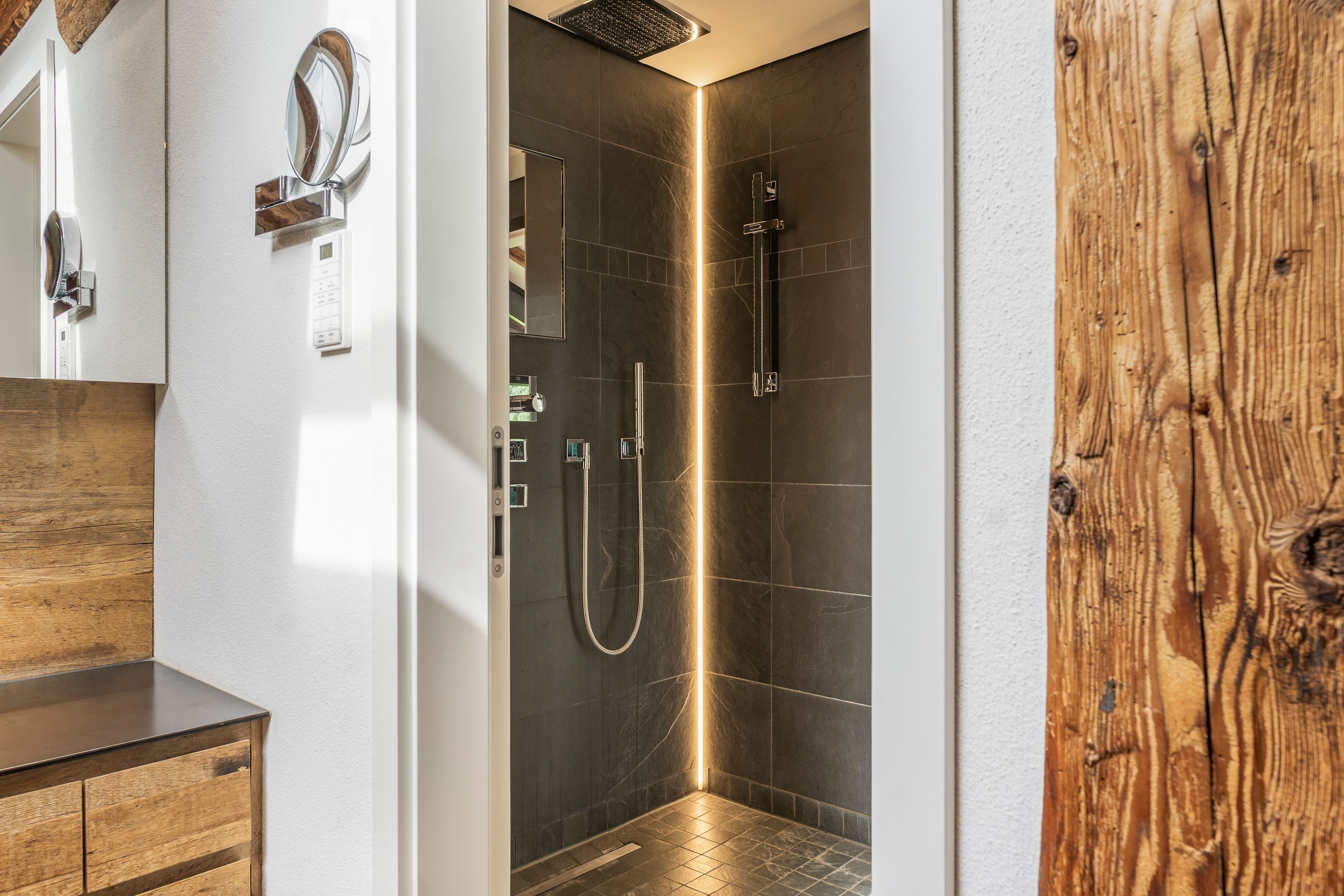 Een moderne badkamer met een douche, een houten wastafelmeubel en een spiegel.