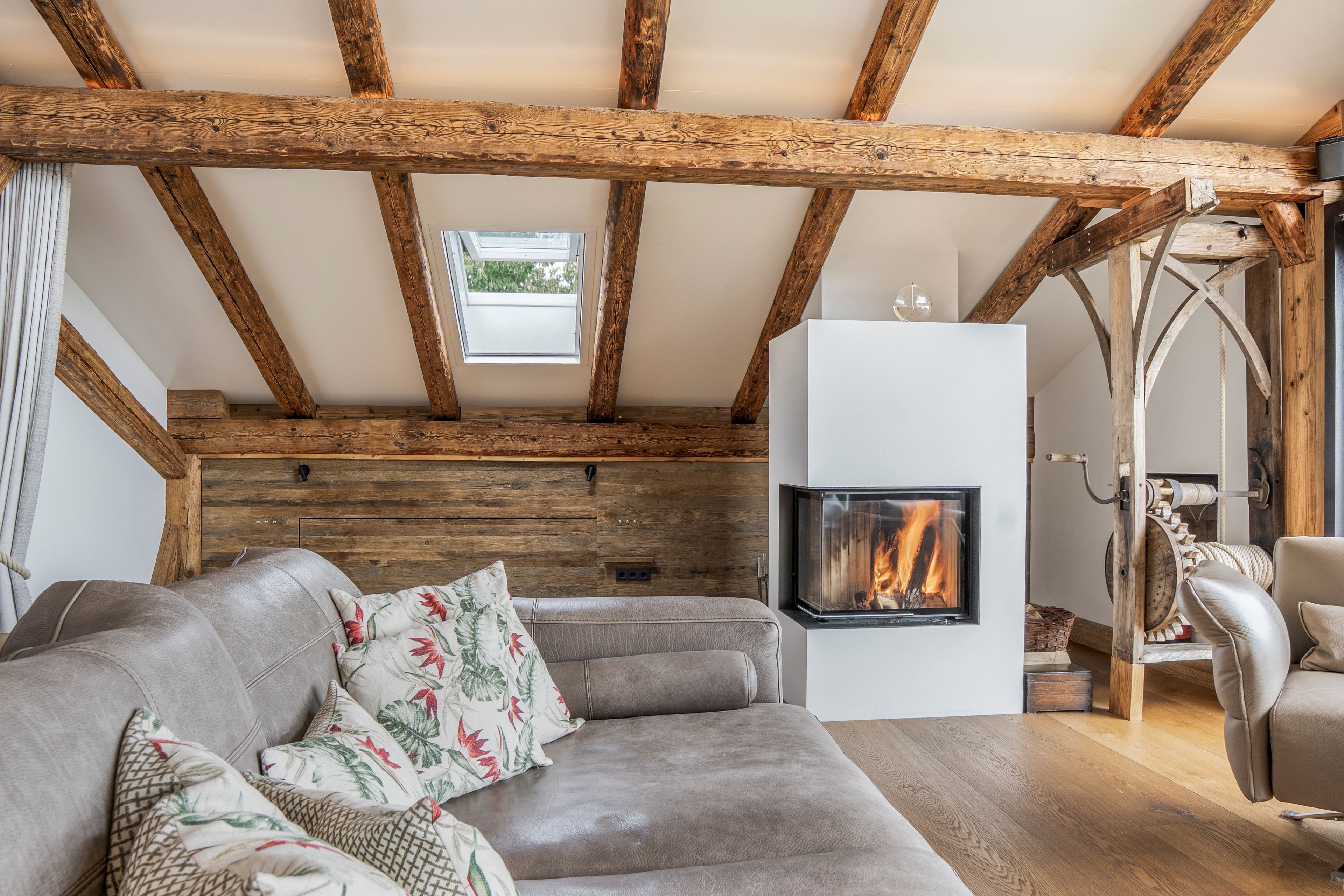 Een gezellige woonkamer met een open haard, houten balken en een moderne bank.