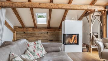 Een gezellige woonkamer met een open haard, houten balken en een moderne bank.