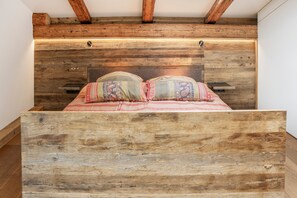 A wooden bed with a headboard in a room with exposed beams.