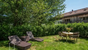 A garden with outdoor furniture and a table, surrounded by lush greenery and a building with a tiled roof.