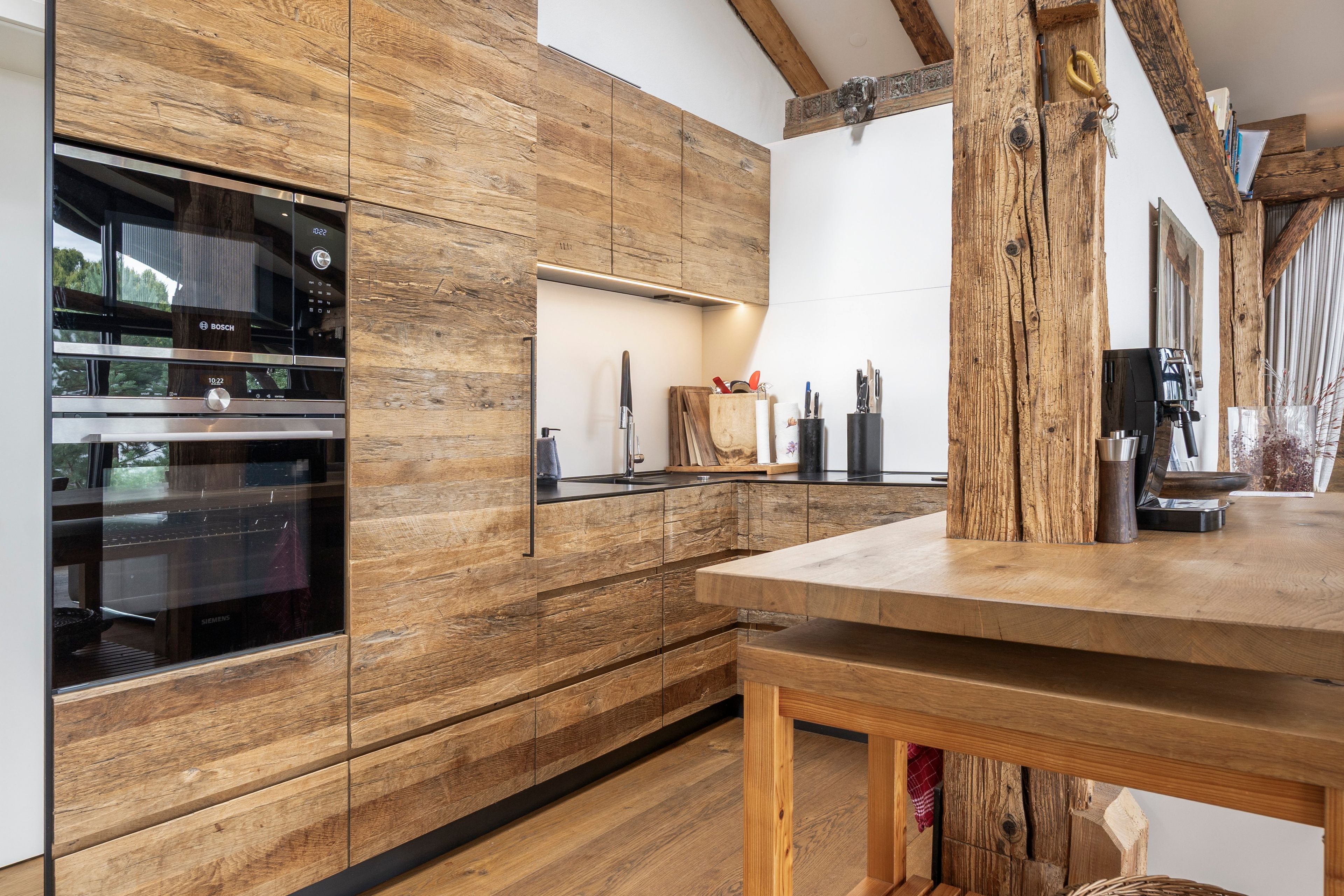 Eine moderne Küche mit Holzschränken, Edelstahlgeräten und einem Holzes Esstisch.