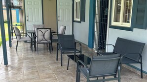 A covered patio area with tiled flooring, metal-framed chairs, a small table, and a door with a window.