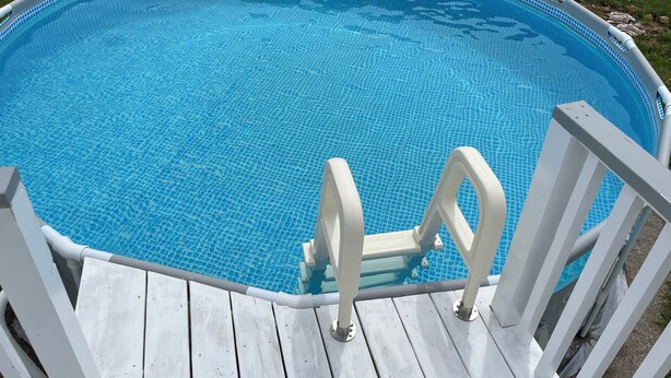 A clear blue swimming pool with a wooden deck and white railings.