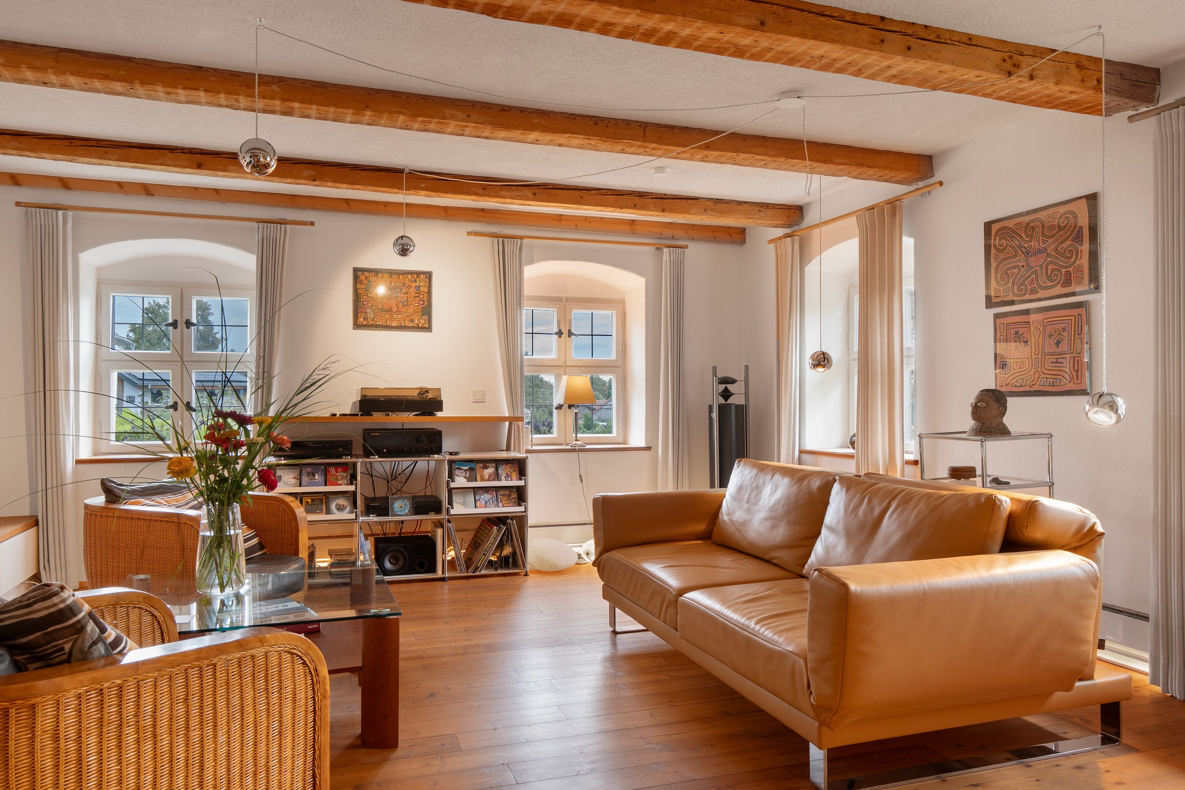 Ein Wohnzimmer mit einer Ledersofa, einem Glastisch, einem Bücherregal und einem großen Fenster mit Vorhängen.