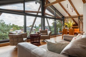 A spacious living room with large windows, a wooden ceiling, and a modern sofa set.