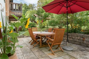 Eine Terrassengruppe im Freien mit Tisch und Stühlen, umgeben von Blumentöpfen und einem roten Sonnenschirm.