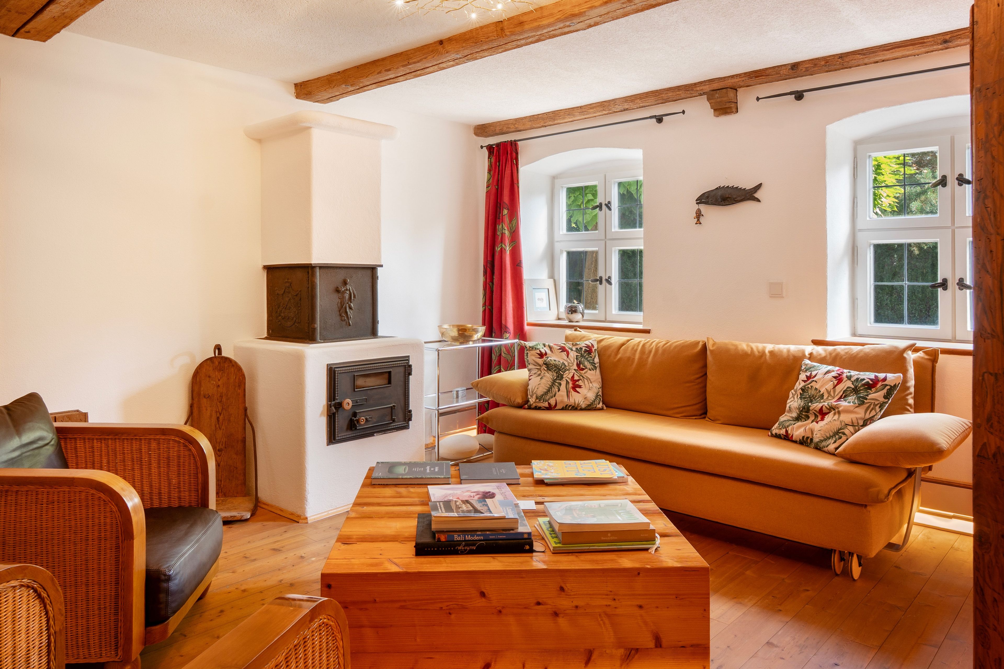 A cozy living room with a sofa, a wooden coffee table with books, a fireplace, and a window with a view of greenery.