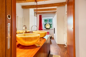 A bathroom with wooden beams, a large window with a view of greenery, and two large yellow sinks.