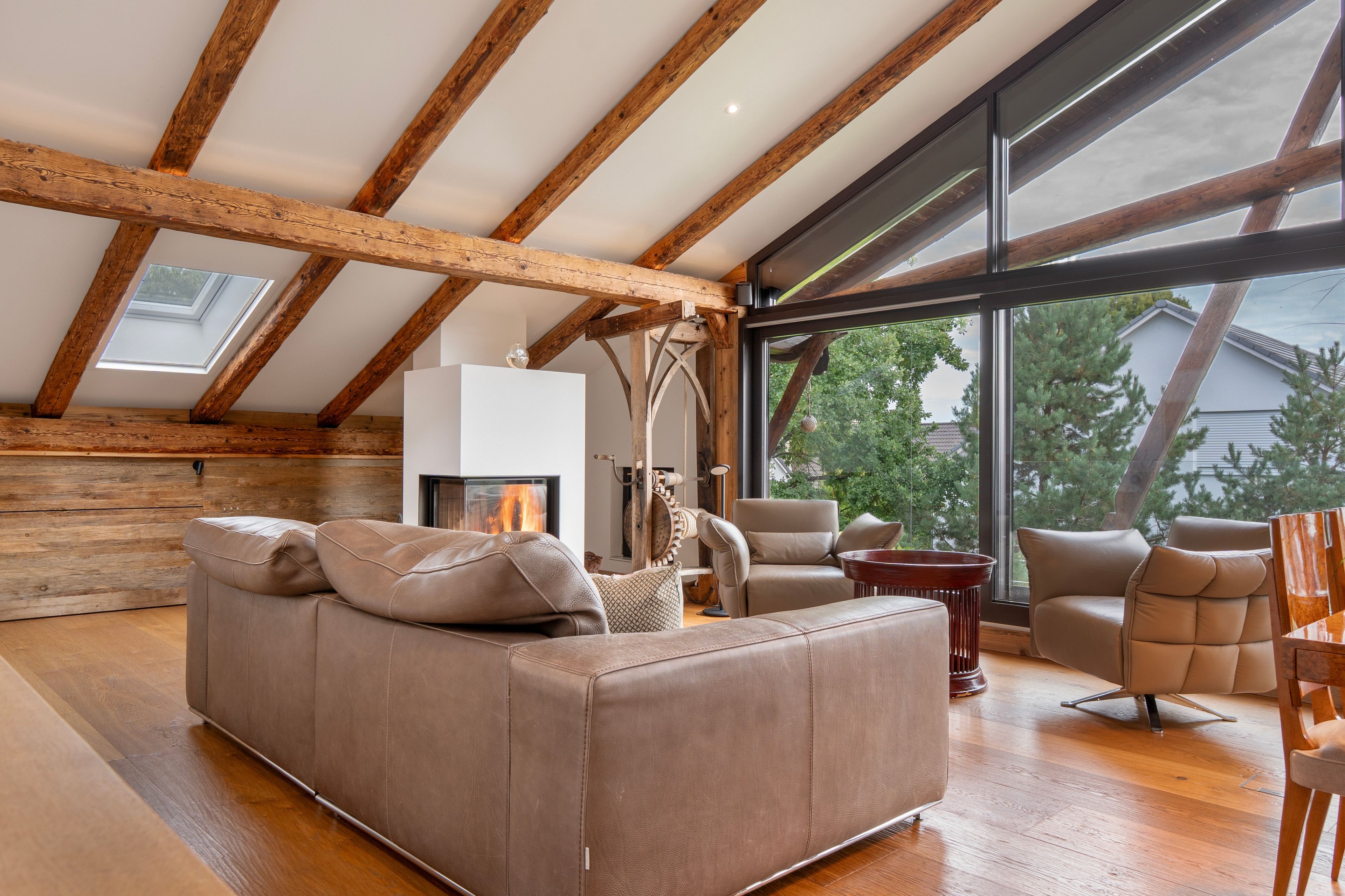 Una sala de estar amplia con techo alto, vigas de madera, chimenea y ventanas grandes que ofrecen vistas al exterior.