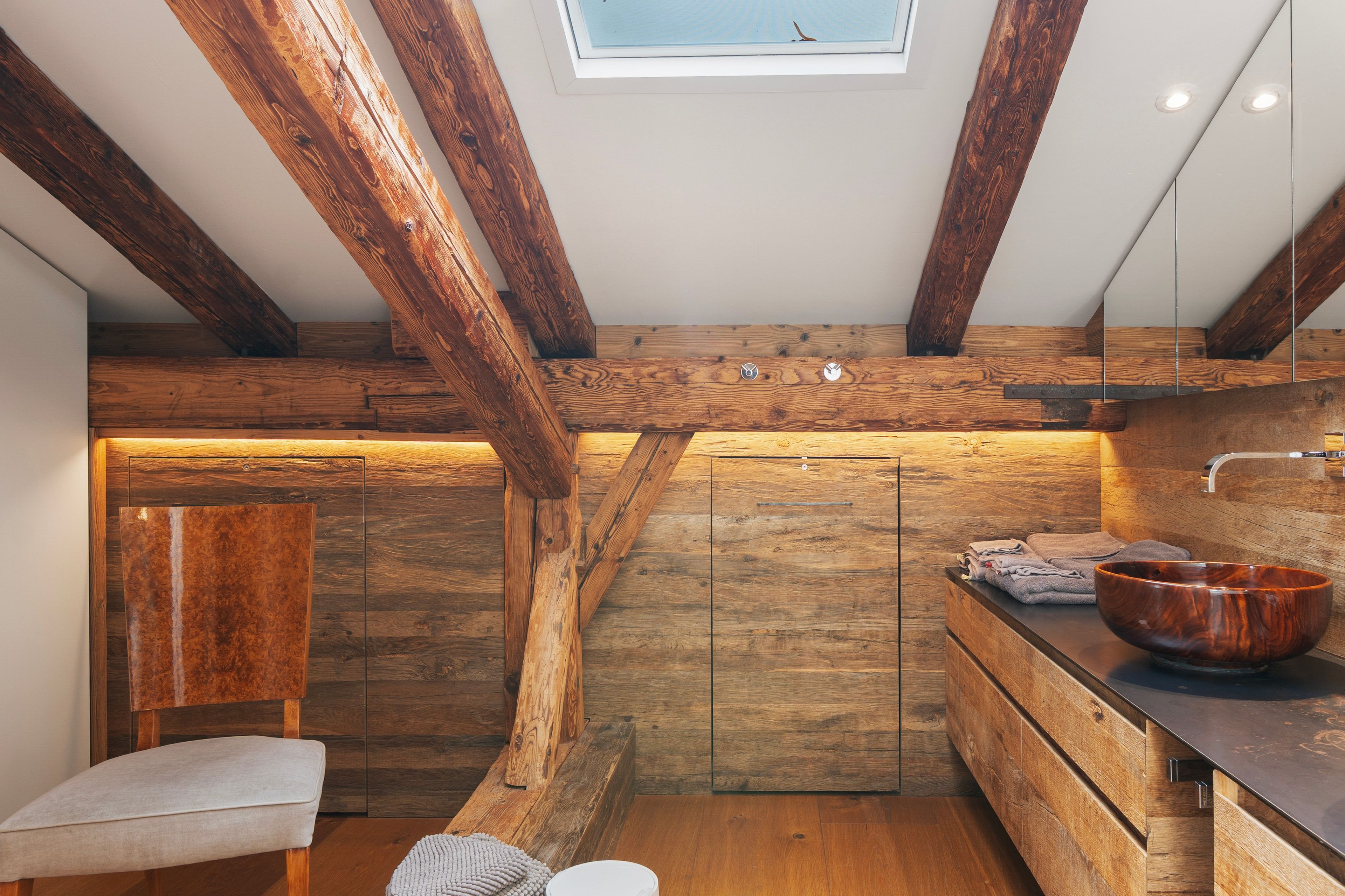 Ein rustikales Badezimmer mit sichtbaren Holzbalken, einer Steinwand und einem Holzbecken.