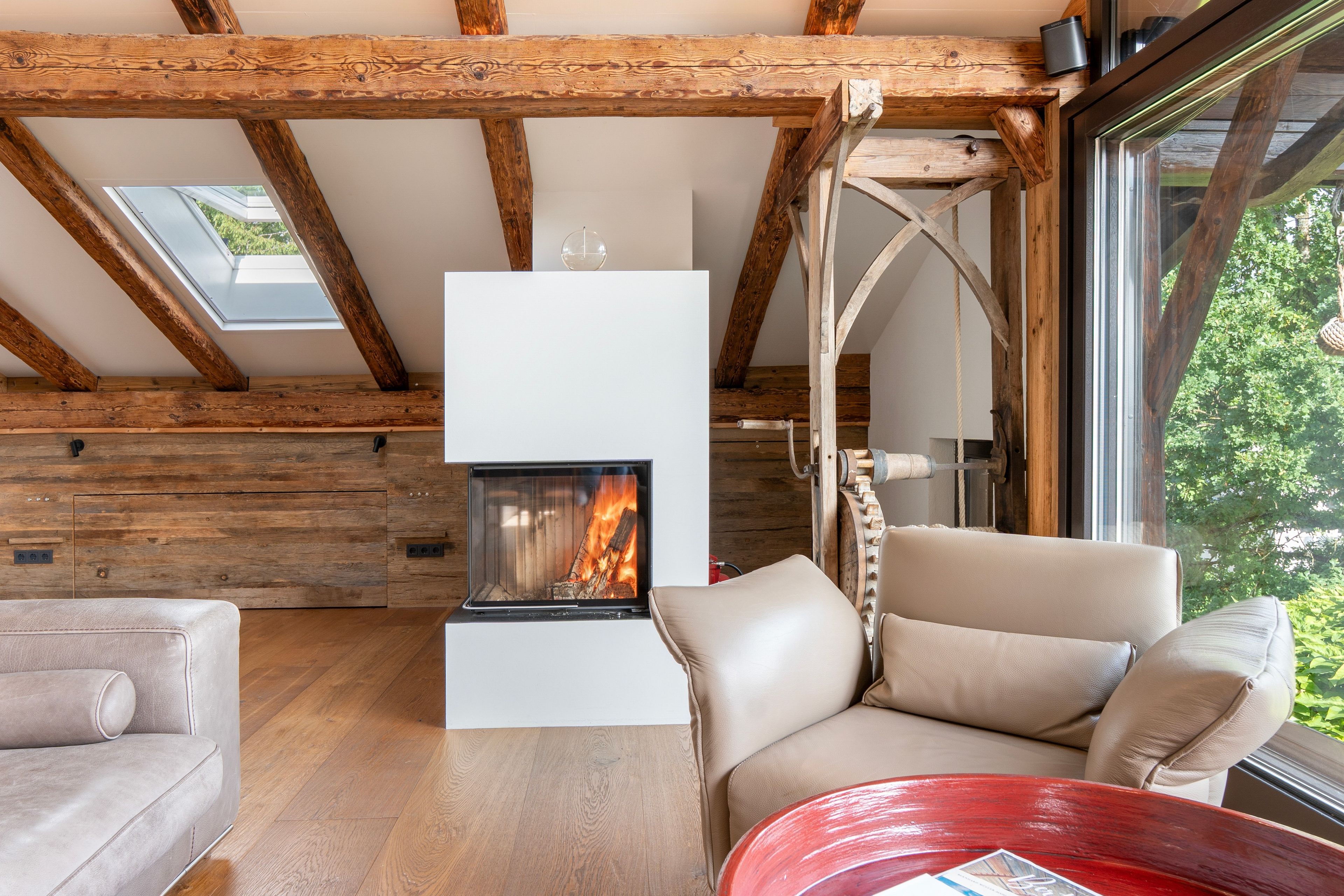 Ein gemütliches Zimmer mit Kamin, Holzbalken, einer Couch und einem Tisch.