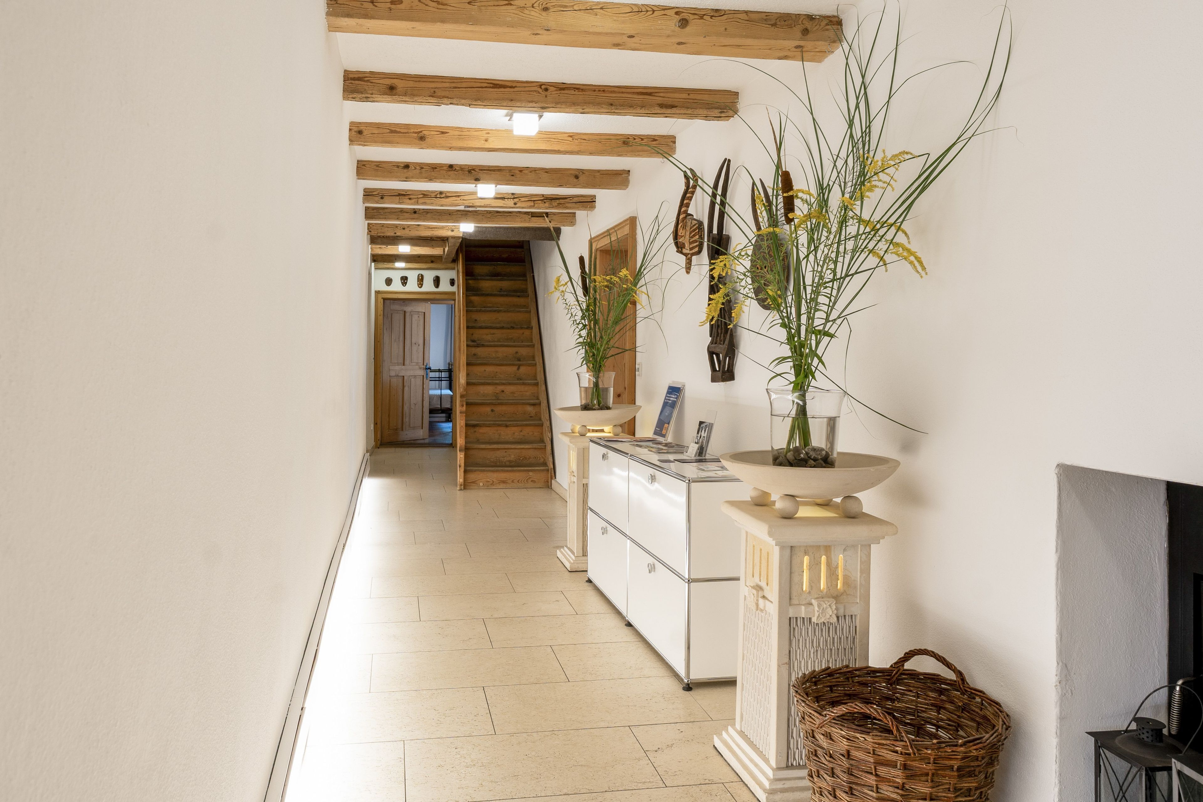 A hallway with wooden beams, a staircase, a kitchen area, and a decorative wall with plants.